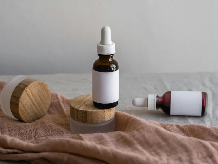a bottle of essential oil next to a wooden container, by Emma Andijewska, trending on pexels, white and pink cloth, surgical iv drip, silicone skin, round format