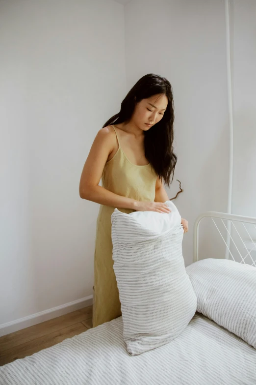 a woman is putting pillows on a bed, inspired by Li Di, wearing a long dress, striped, full product shot, honey