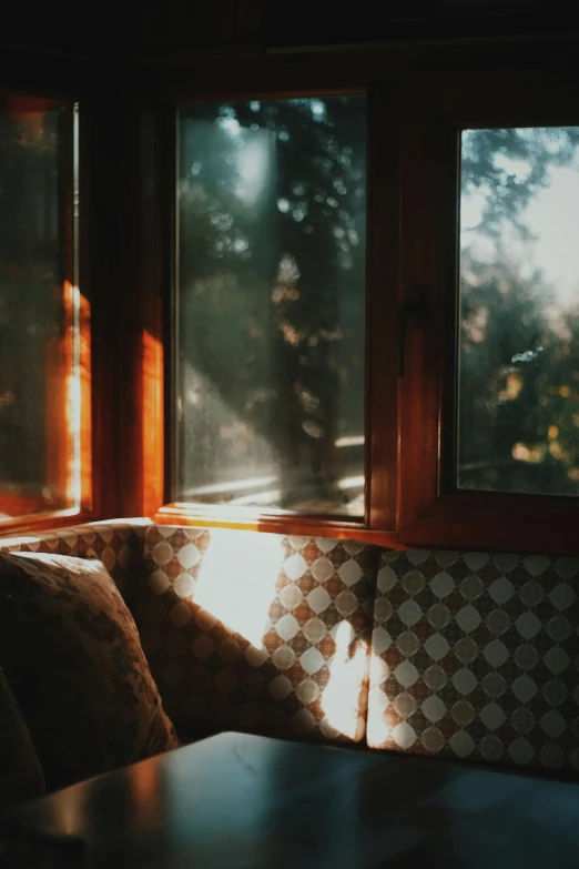 a couch sitting in front of a window next to a table, inspired by Elsa Bleda, unsplash contest winner, romanticism, sun shafts, dappled in evening light, cozy wallpaper, during autumn