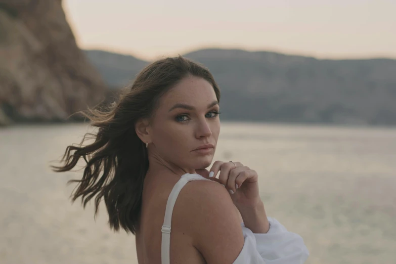 a woman standing in front of a body of water, camilla luddington, portrait image, hills, (golden hour)