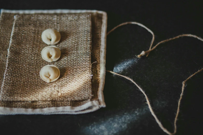 a pair of buttons sitting on top of a burlock bag, a macro photograph, inspired by Albert Anker, unsplash, served with pasta, hessian cloth, in a row, bells