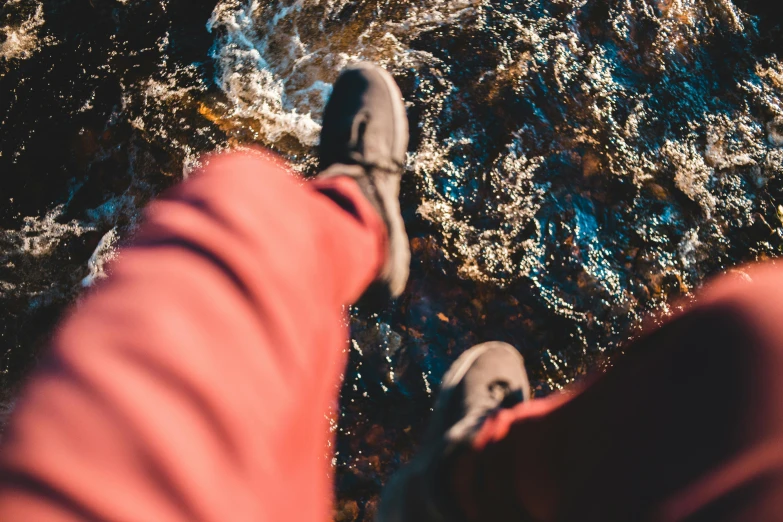 a person standing next to a body of water, detailed shot legs-up, wearing adventure gear, slightly red, thumbnail