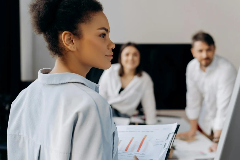 a woman holding a piece of paper in front of a group of people, trending on pexels, female in office dress, looking off to the side, black female, charts