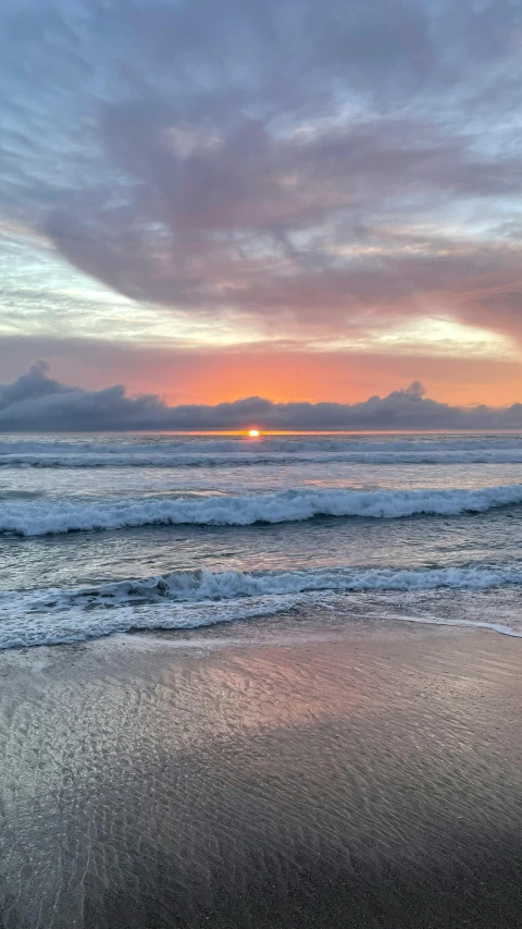 a man riding a surfboard on top of a sandy beach, during a sunset