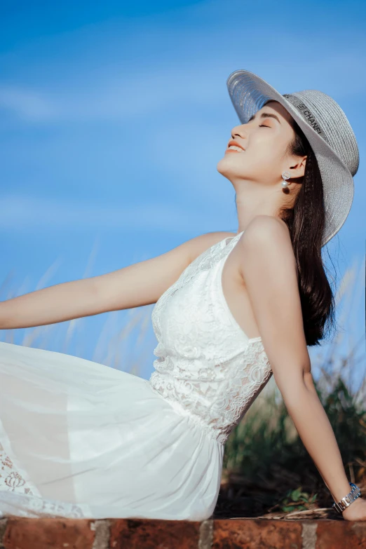 a woman in a white dress and hat sitting on a brick wall, by Tan Ting-pho, pexels contest winner, clear blue sky vintage style, li bingbing, sundress, closeup - view