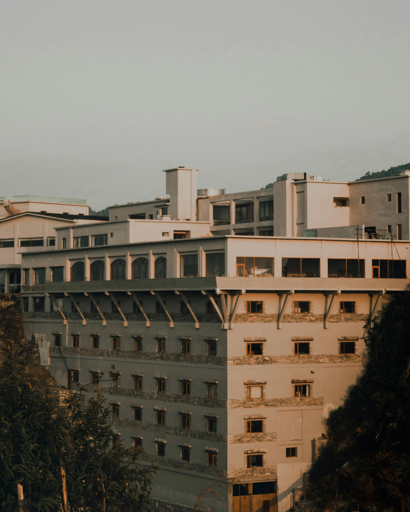 a tall building sitting on top of a lush green hillside, inspired by Elsa Bleda, unsplash contest winner, brutalism, abandoned hospital, crenellated balconies, private school, sits on a rooftop