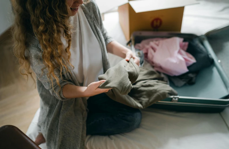 a woman sitting on top of a bed next to a suitcase, by Alice Mason, pexels contest winner, happening, sustainable materials, exiting from a wardrobe, packaging, australian