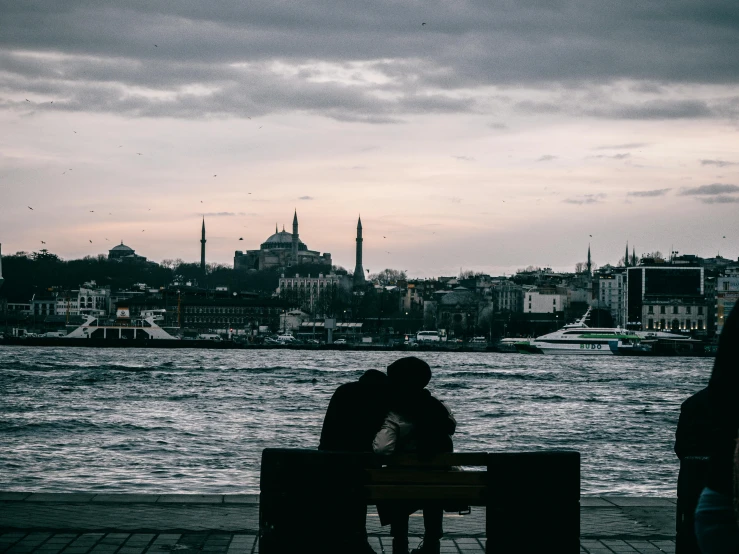 two people sitting on a bench in front of a body of water, pexels contest winner, hurufiyya, the fall of constantinople, making out, building in the distance, youtube thumbnail