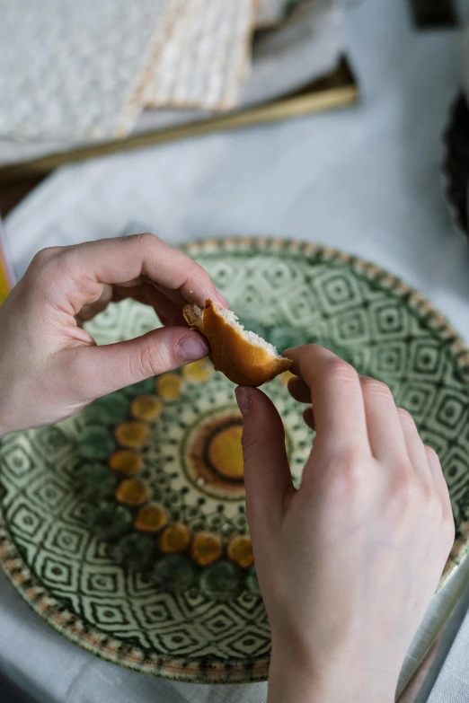 a person holding a piece of bread on a plate, intricate design, caramel, eats bambus, tabletop