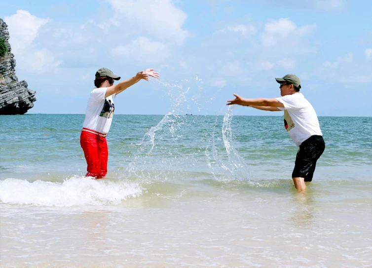 a couple of men standing on top of a beach next to the ocean, splashing water, floating in water, profile image