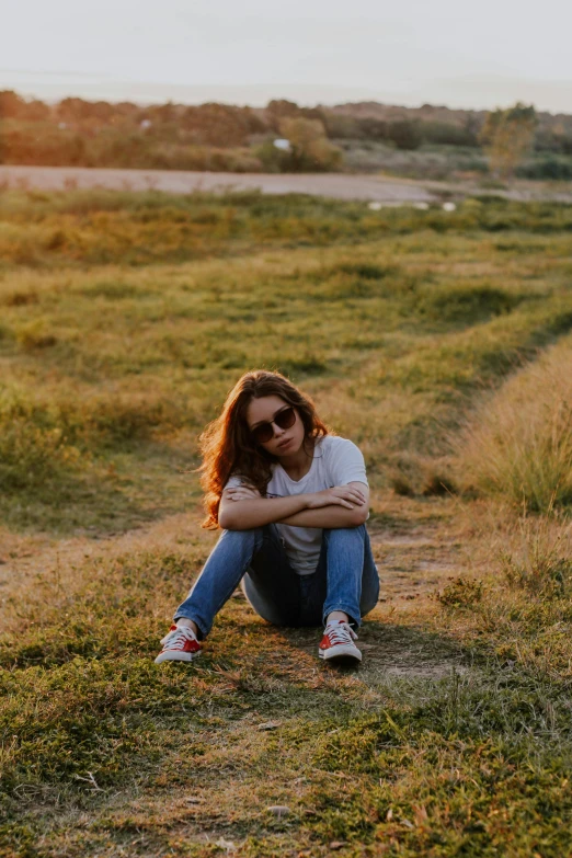 a woman sitting on top of a grass covered field, wearing orange sunglasses, wearing white sneakers, 2019 trending photo, soft evening lighting