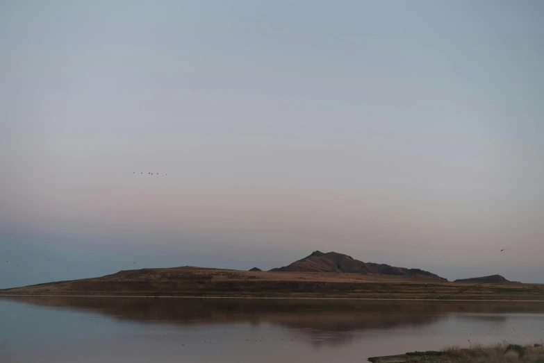 a body of water with a mountain in the background, unsplash, land art, birds flying in the distance, twilight ; wide shot, mongolia, archival pigment print