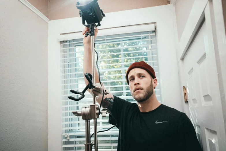 a man holding up a camera on a tripod, a portrait, by Ryan Pancoast, unsplash, photorealism, surgery, still from a music video, tall forehead, home video footage