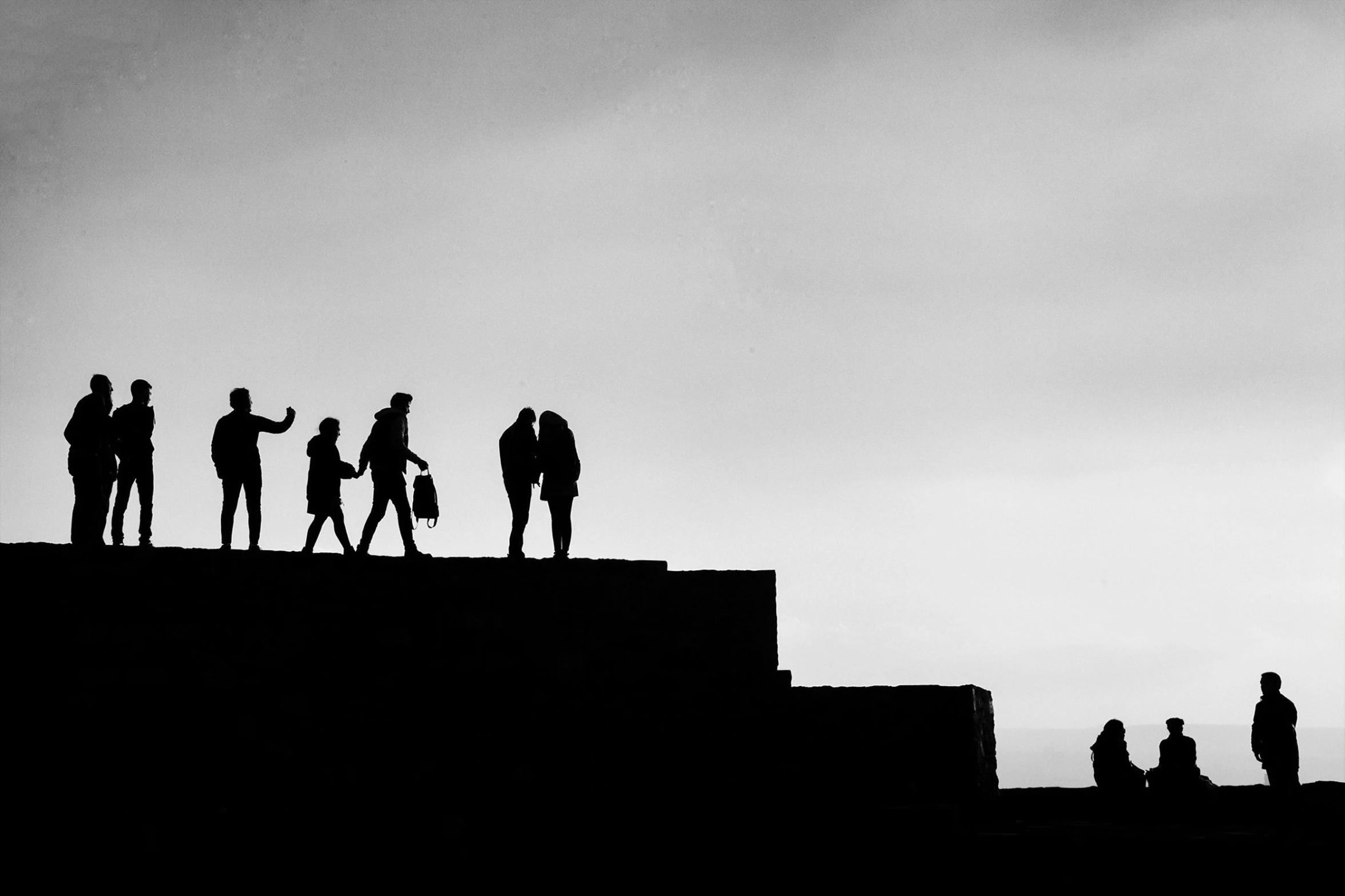 a group of people standing on top of a hill, a black and white photo, by Gusztáv Kelety, pexels contest winner, silhouette!!!, family framed on the wall, friendship, stairway to heaven