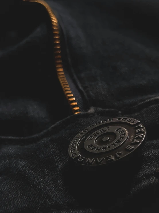 a close up of a button on a jacket, inspired by Eugène Brands, unsplash, black extremely tight jeans, ((gears)), high angle shot, carbon black and antique gold