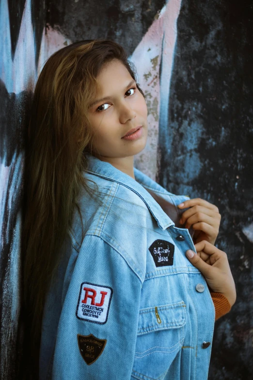 a woman standing in front of a graffiti covered wall, an album cover, by Ric Estrada, instagram, pop art, denim jacket, model エリサヘス s from acquamodels, teenager girl, portrait emily ratajkowski