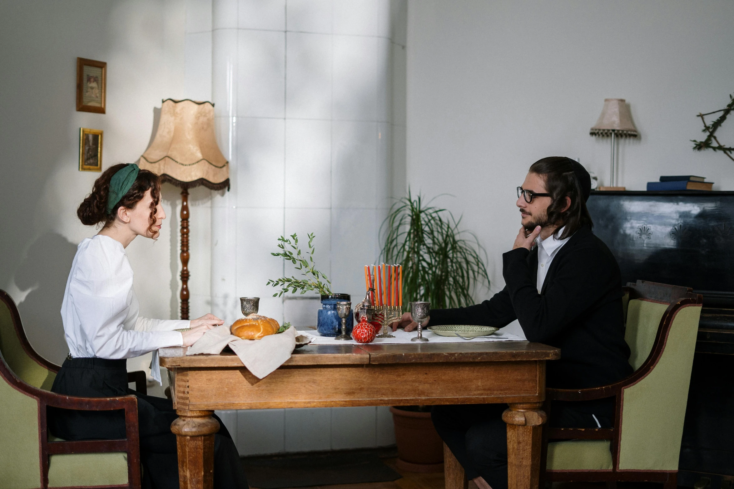 a man and a woman sitting at a table, by Emma Andijewska, unsplash, renaissance, jewish young man with glasses, production still, chef table, wooden desks with books