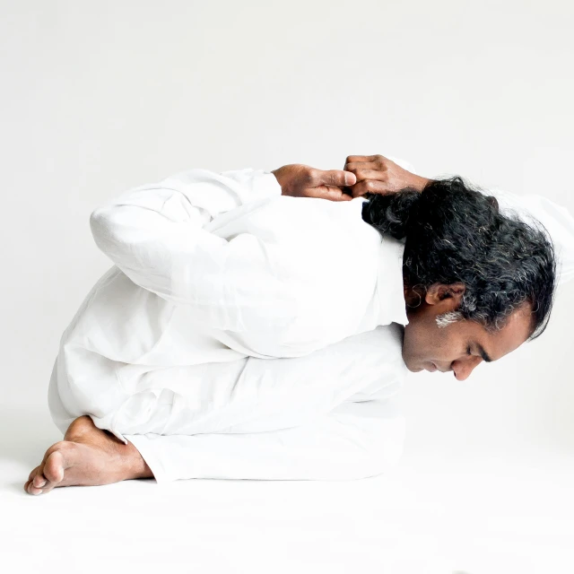 a man sitting on the ground with his hands on his head, in white turtleneck shirt, anjali mudra, white backdrop, wearing white robes