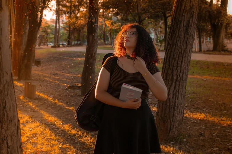 a woman standing in a park holding a book, by Carey Morris, pexels contest winner, sun down, tall female emo art student, black, ariel perez