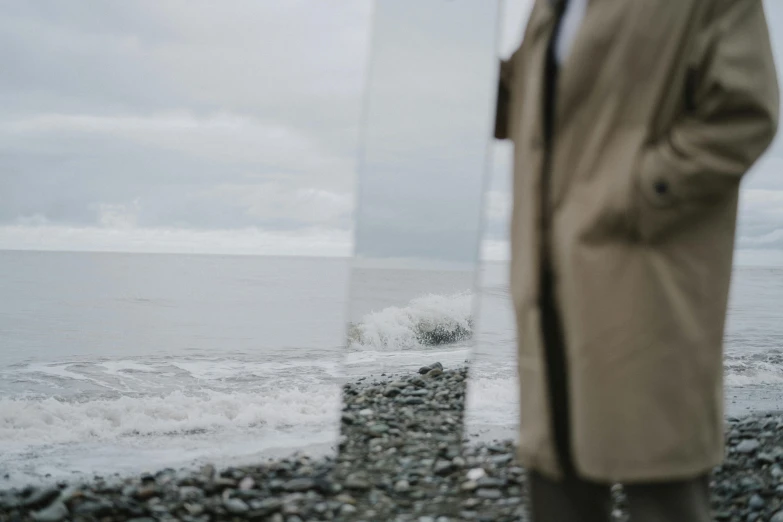 a man standing on a beach next to a body of water, visual art, mirror and glass surfaces, overcast weather, close - up photograph, julia hetta