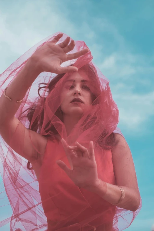 a woman in a red dress with a veil over her head, an album cover, pexels contest winner, the sky is pink, warpaint aesthetic, a redheaded young woman, hands in air