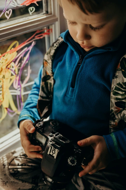 a young boy holding a camera in front of a window, visual art, light tracing, camera looking down into the maw, switch, multicoloured