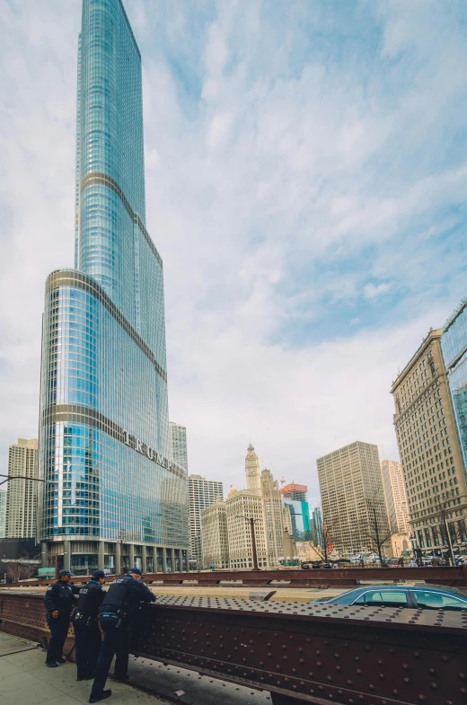 a group of people standing in front of a tall building, chicago skyline, trump tower, from the distance, plaza