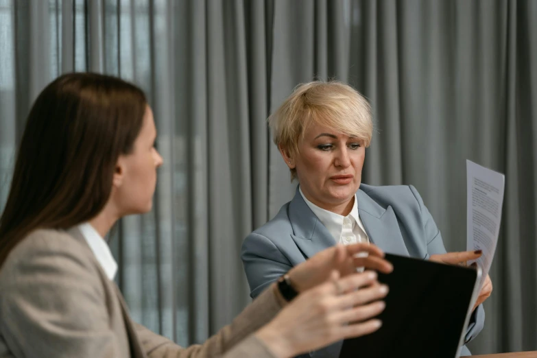 two women sitting at a table with papers in front of them, by Emma Andijewska, pexels contest winner, hurufiyya, looking her shoulder, lawyer, paul barson, slightly minimal