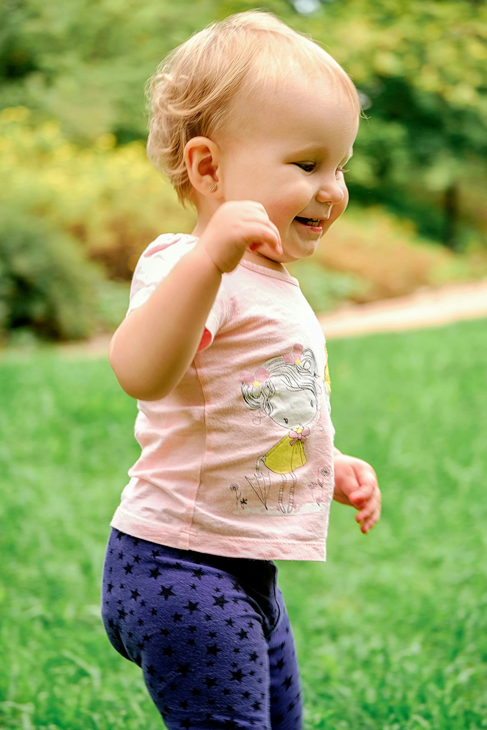 a little girl standing on top of a lush green field, a picture, inspired by Margaret Geddes, happening, wearing pants and a t-shirt, she is smiling and excited, walking at the garden, tiny stars