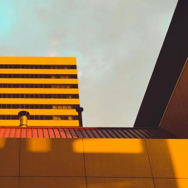 a yellow building with a blue sky in the background, inspired by Beeple, unsplash contest winner, brutalism, sun and shadow over a city, orange and teal color, high-angle, dimly - lit