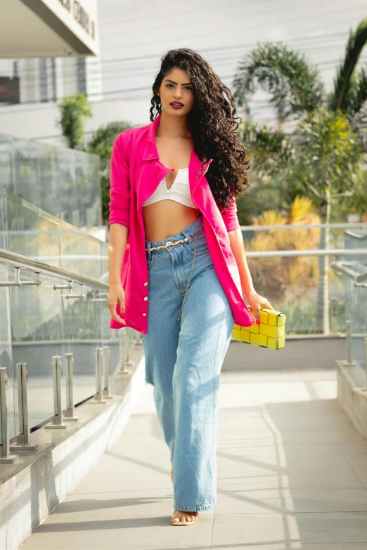 a woman walking down a sidewalk carrying a yellow purse, an album cover, by Max Dauthendey, instagram, pop art, indian super model, cropped shirt with jacket, vibrant pink, with long curly hair