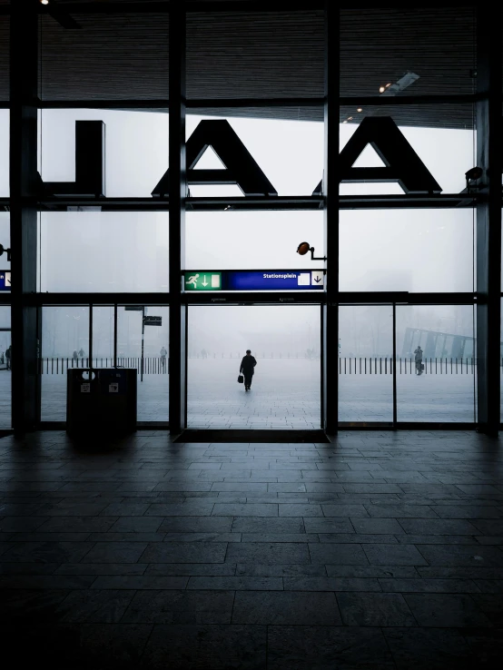 a person standing in front of a large window, a picture, inspired by Andreas Gursky, unsplash contest winner, black. airports, ground covered in mist, amsterdam, about to enter doorframe