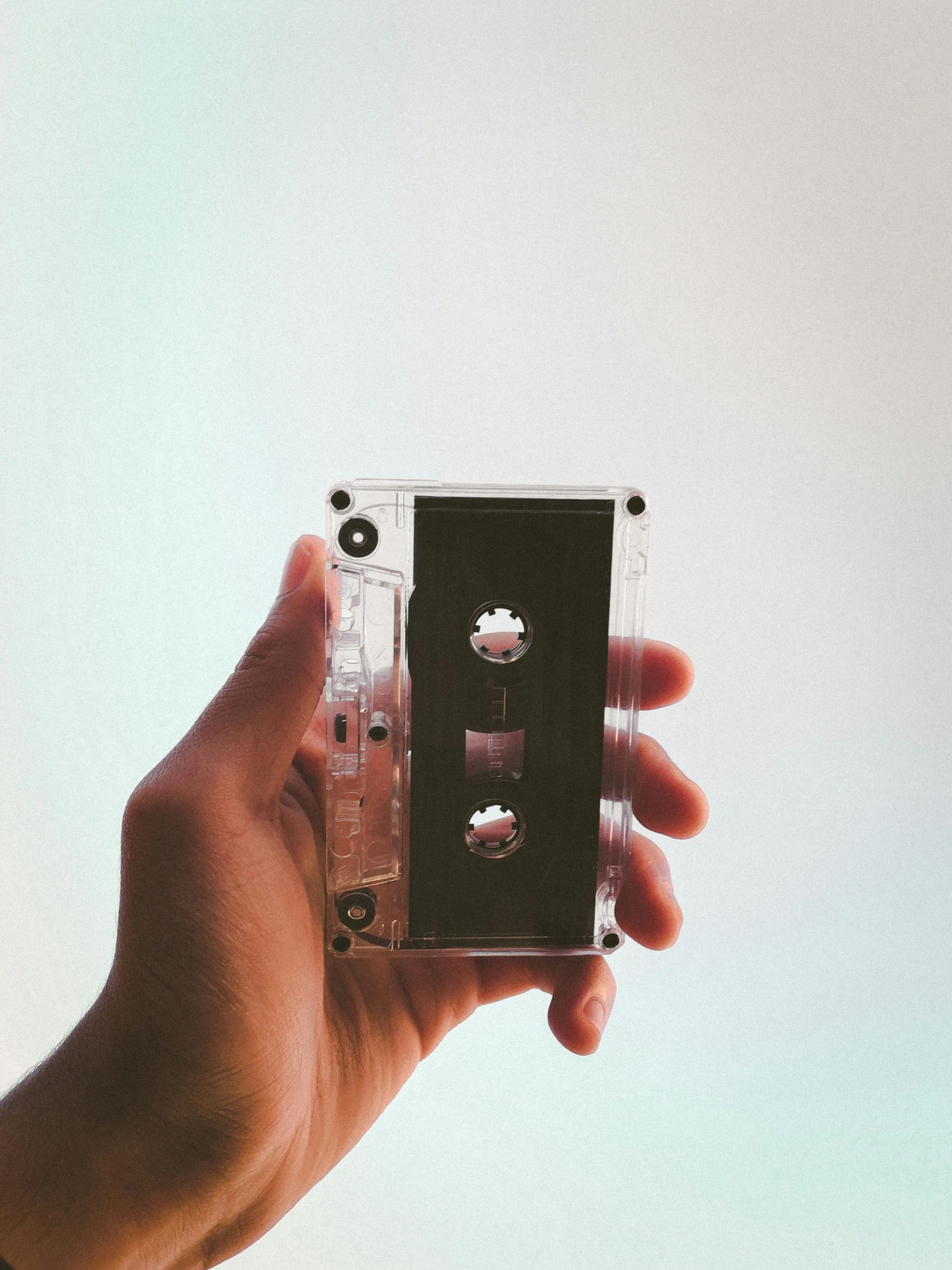 a person holding a cassette in their hand, trending on pexels, translucent body, tall shot, promo image, back - shot