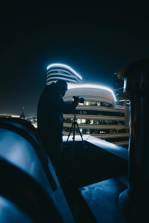 a man standing on top of a roof next to a camera, by Ryan Pancoast, unsplash contest winner, neon city domes, car shot, behind the scenes, busy night