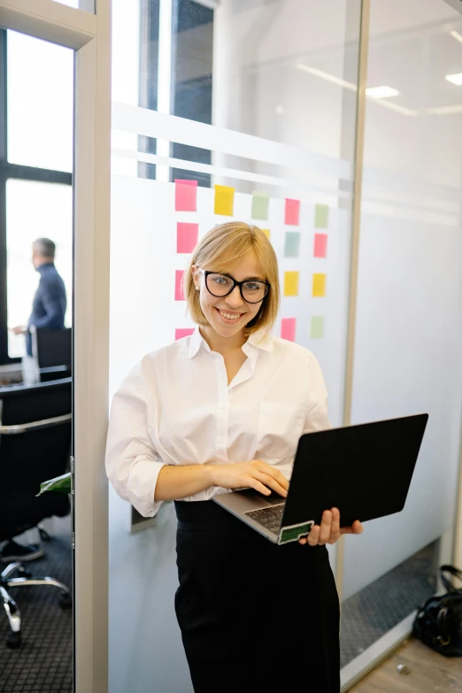 a woman standing in an office with a laptop, by Oskar Lüthy, pexels contest winner, wearing black rimmed glasses, vp of marketing, sebastian ludke, programming