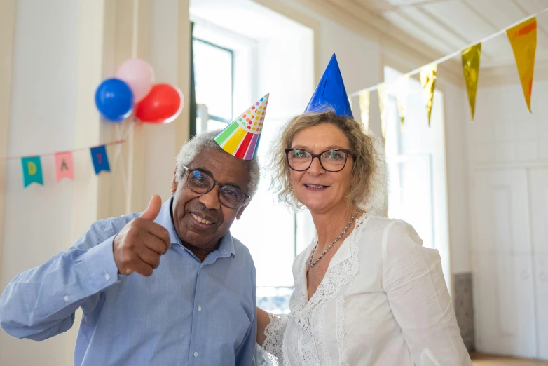 a man and woman standing next to each other at a party, pexels contest winner, wearing a party hat, elderly, thumb up, malcolm hart