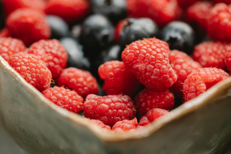 a bowl filled with raspberries and blueberries, unsplash, ilustration, close-up photo, 2000s photo, fan favorite