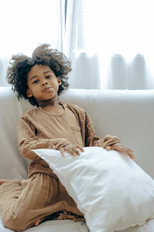 a little girl sitting on a couch with a pillow, pexels, portrait of willow smith, muted brown, stockphoto, game ready