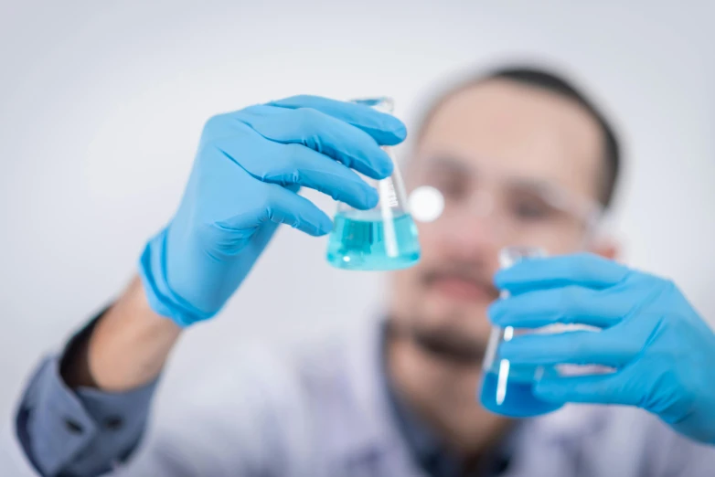 a man in a lab coat and blue gloves holding a flask, a picture, shutterstock, hazy, technologies, profile picture, blue