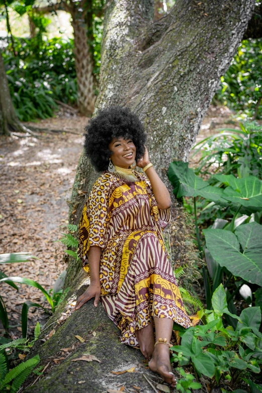 a woman sitting on a log next to a tree, by Lisa Milroy, pexels contest winner, afrofuturism, patterned clothing, in louisiana, big hair, lush surroundings