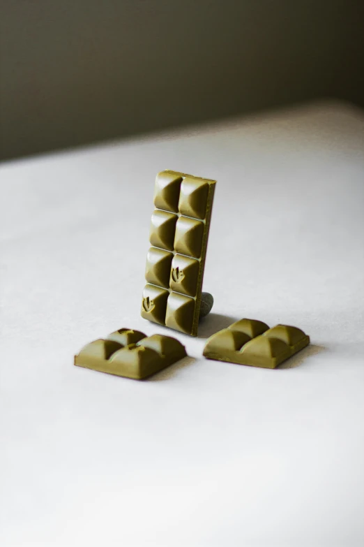 a couple of pieces of chocolate sitting on top of a table, a picture, olive green, 3 d print, hemp, studs