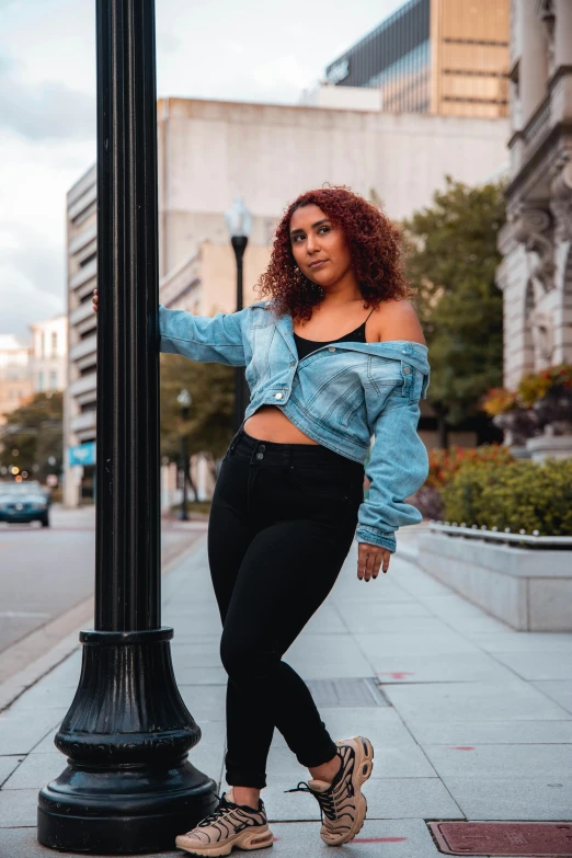 a woman leaning against a lamp post on a city street, an album cover, by Matt Cavotta, trending on pexels, renaissance, wearing a jeans jackets, full figured, wearing a crop top, striking a pose