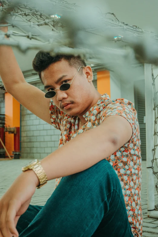 a man sitting on the ground wearing sunglasses, an album cover, inspired by Eddie Mendoza, trending on pexels, crossed arms, batik, non-binary, holding gold watch