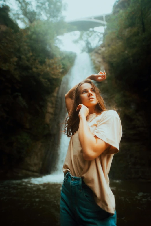 a woman standing in front of a waterfall, a polaroid photo, inspired by Elsa Bleda, renaissance, brown hair flow, trending photo, light falling on face, casual pose