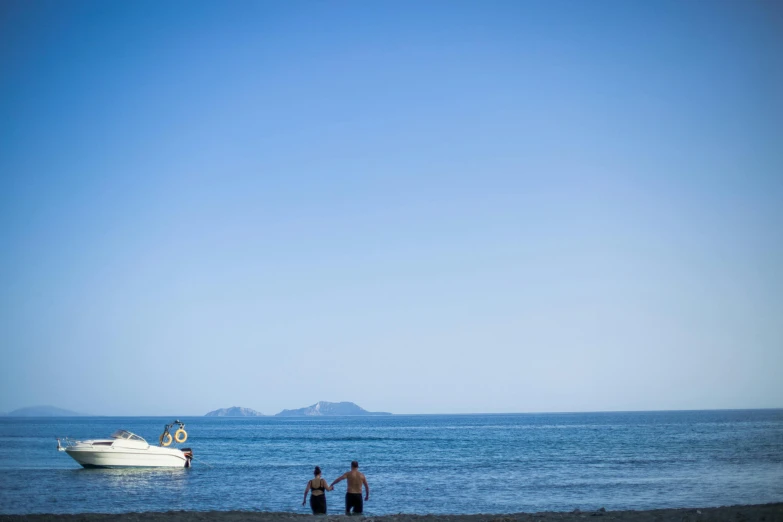 a couple of people that are standing in the water, by Peter Churcher, unsplash, clear blue skies, te pae, gulf of naples, from a distance