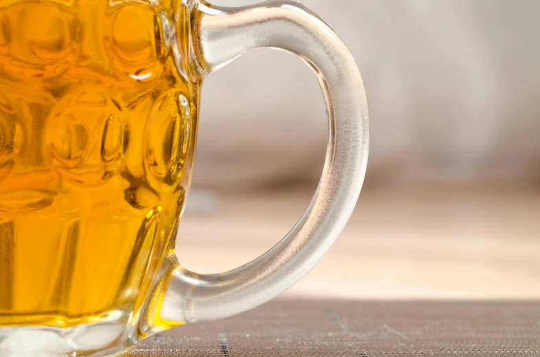 a glass of beer sitting on top of a wooden table, unsplash, photorealism, holding a tankard of ale, macro detail, yellow, zoom shot