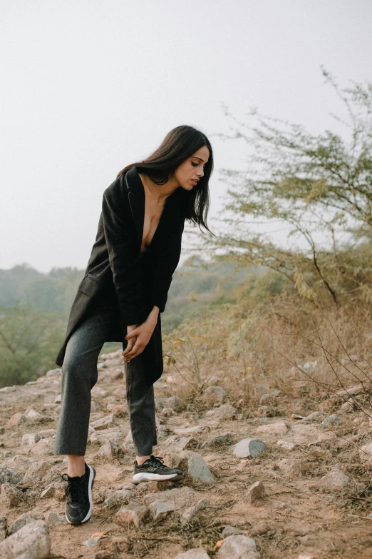 a woman standing on top of a rocky hill, trending on pexels, black loafers, provocative indian, worn black coat, portrait image