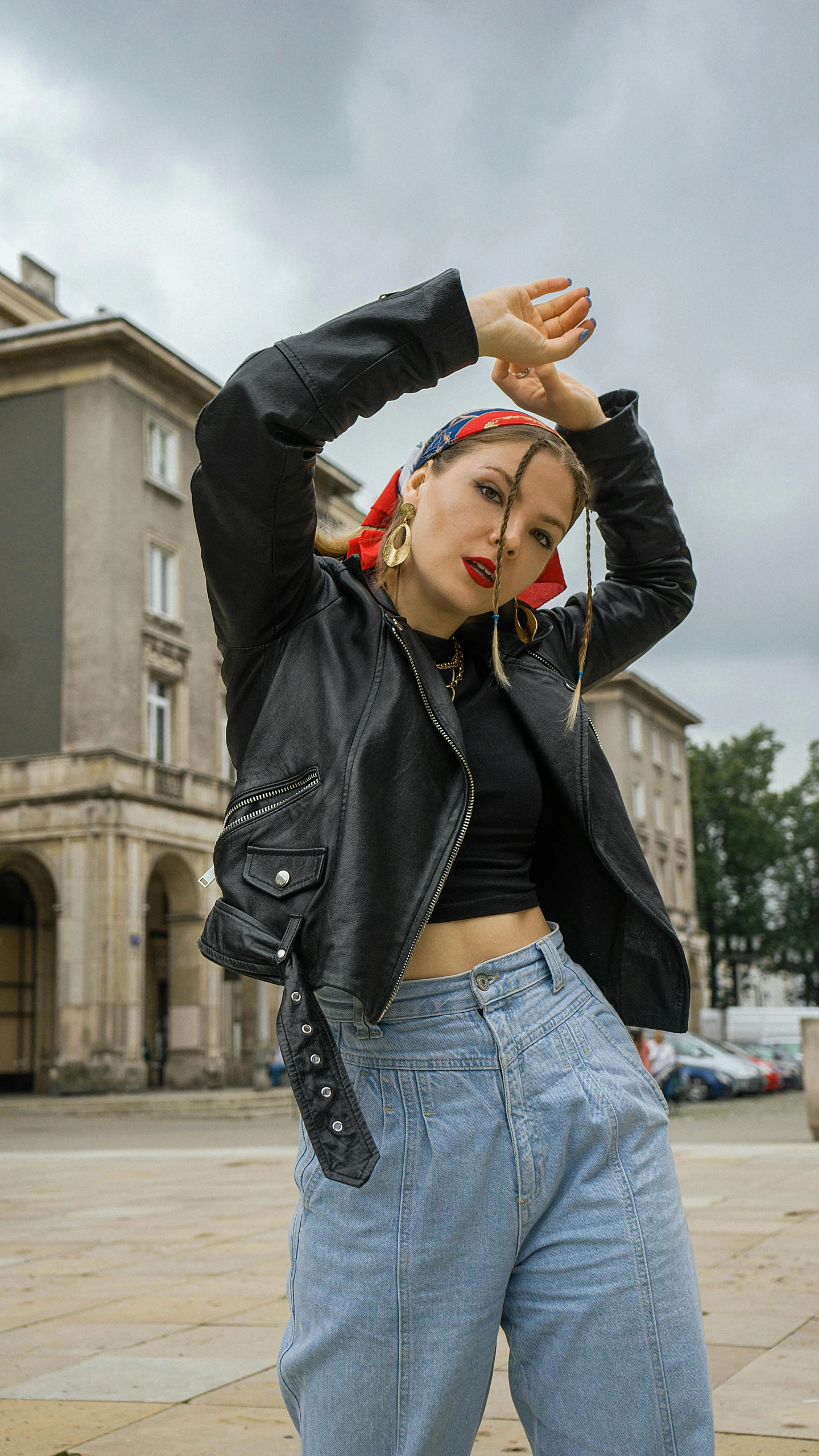 a woman posing for a picture in front of a building, an album cover, by Emma Andijewska, trending on pexels, graffiti, red bandana, in an old 1950s leather jacket, classic dancer striking a pose, 15081959 21121991 01012000 4k