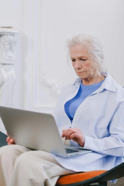 a woman sitting in a chair using a laptop computer, trending on reddit, diagnostics, looking old, wearing a grey robe, on a pale background