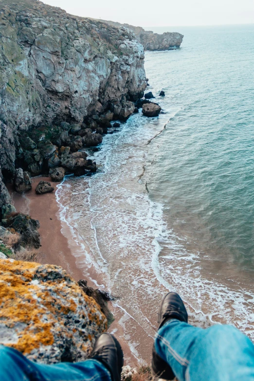 a person sitting on top of a cliff next to the ocean, omaha beach, body of water, from above, unsplash 4k